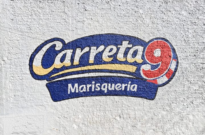 Mural del logotipo de Carreta 9 Marisquería pintado en azul, amarillo y rojo sobre una pared blanca texturizada